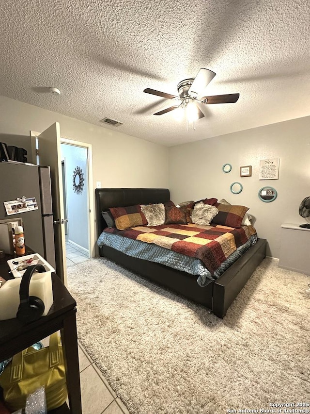 bedroom featuring stainless steel fridge, ceiling fan, light tile patterned floors, and a textured ceiling