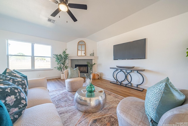 living room featuring wood-type flooring, vaulted ceiling, ceiling fan, and a tiled fireplace