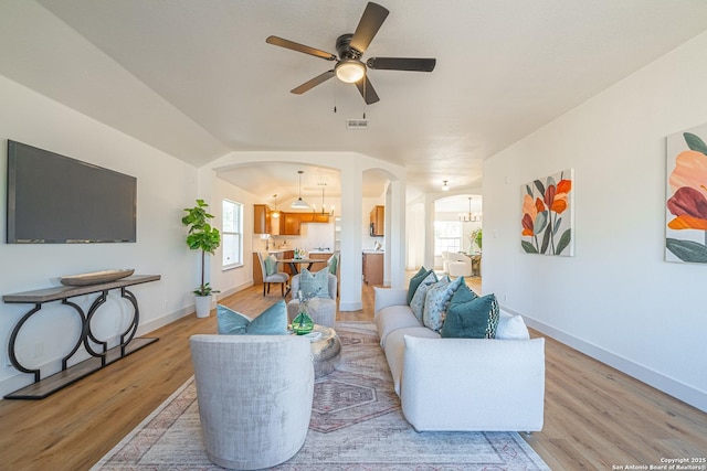 living room featuring ceiling fan with notable chandelier, lofted ceiling, and light hardwood / wood-style flooring