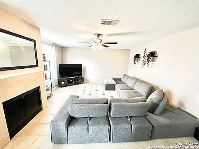 tiled living room with a tile fireplace, ceiling fan, and a textured ceiling