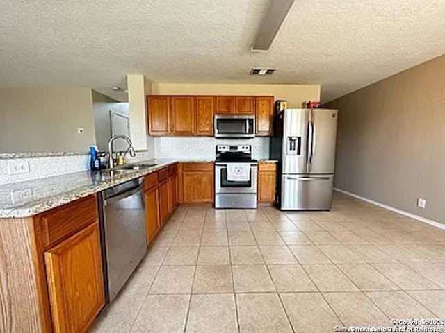 kitchen featuring sink, light stone counters, kitchen peninsula, light tile patterned floors, and appliances with stainless steel finishes