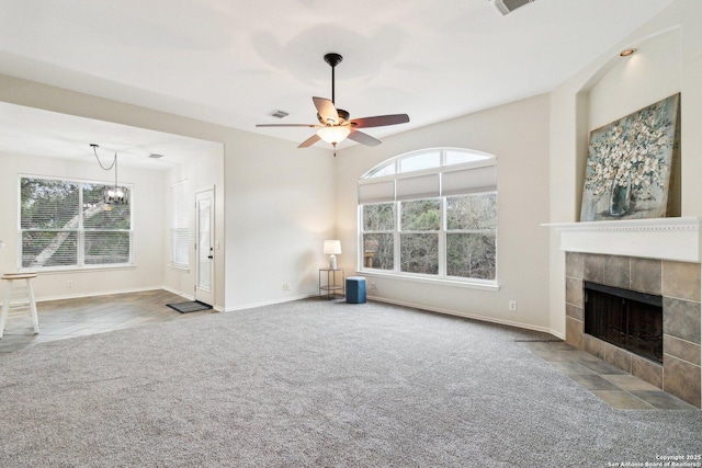 unfurnished living room featuring a tile fireplace, carpet, and ceiling fan with notable chandelier