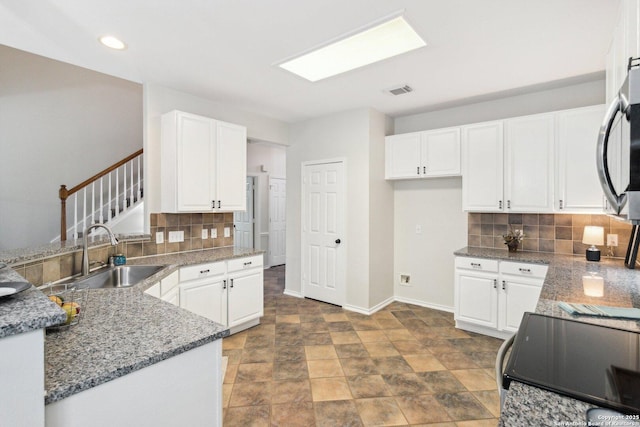 kitchen with stove, tasteful backsplash, white cabinetry, and sink