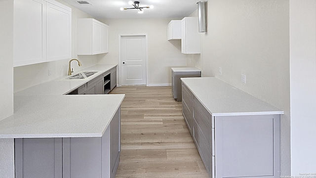 kitchen with sink, white cabinetry, a notable chandelier, light hardwood / wood-style floors, and kitchen peninsula