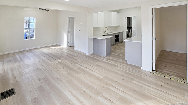 unfurnished living room with ceiling fan, sink, and light hardwood / wood-style flooring