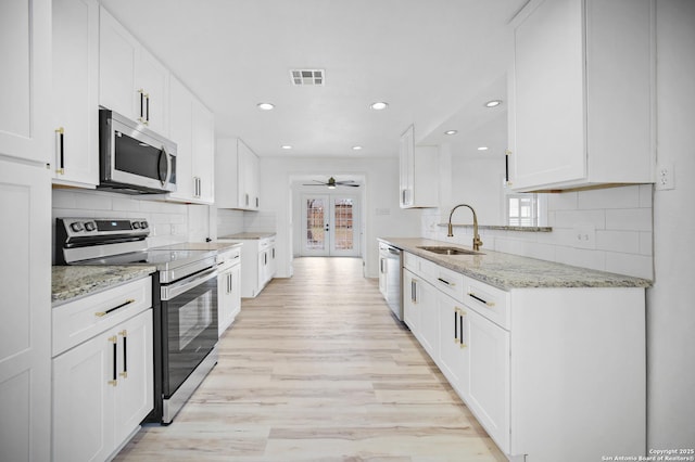 kitchen with a wealth of natural light, white cabinetry, sink, stainless steel appliances, and light stone counters