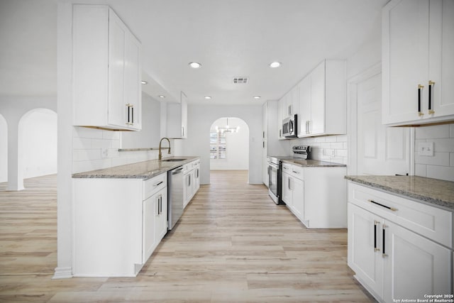 kitchen featuring backsplash, light stone counters, stainless steel appliances, sink, and white cabinetry