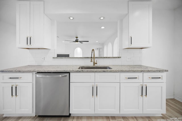 kitchen with stainless steel dishwasher, light stone counters, white cabinets, and sink