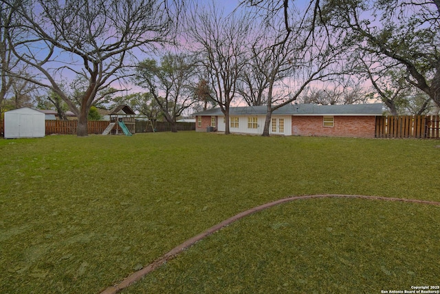 yard at dusk featuring a playground and a storage shed