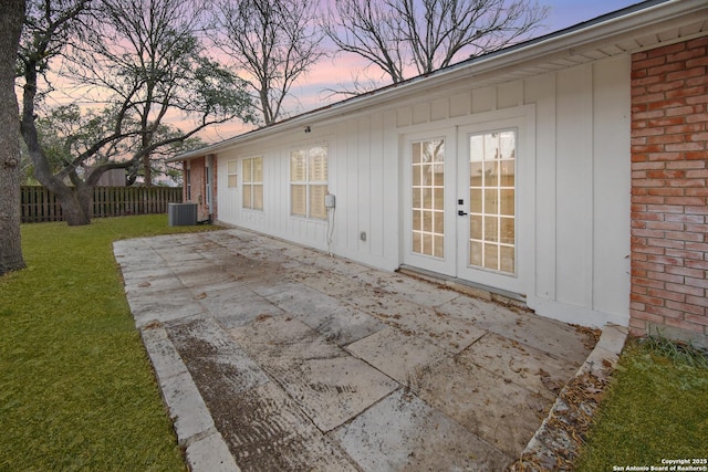 patio terrace at dusk featuring central AC unit, a yard, and french doors