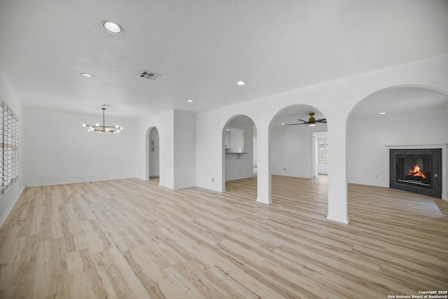 unfurnished living room featuring a fireplace, ceiling fan with notable chandelier, and light hardwood / wood-style floors