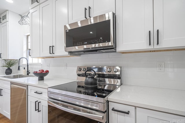 kitchen with white cabinetry, sink, light stone countertops, stainless steel appliances, and tasteful backsplash