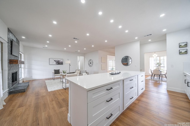 kitchen featuring a stone fireplace, white cabinetry, a center island, and light hardwood / wood-style floors