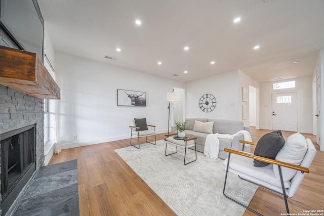 living room with a stone fireplace and light wood-type flooring