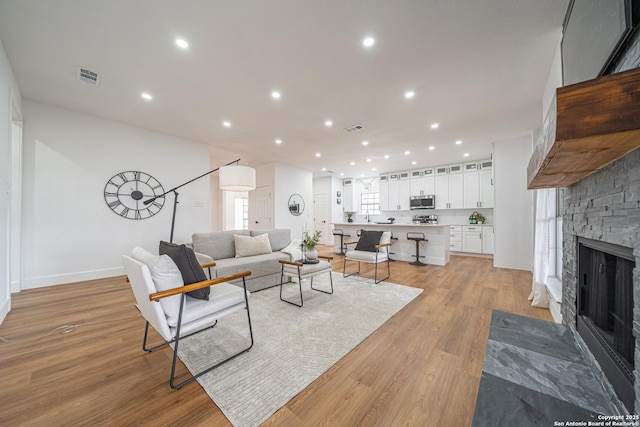 living room with a stone fireplace and light hardwood / wood-style flooring