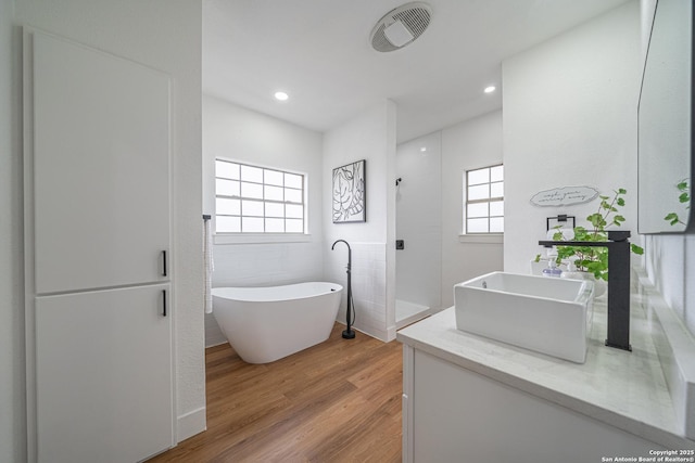 bathroom with hardwood / wood-style floors, vanity, tile walls, and plus walk in shower