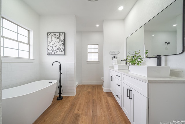 bathroom with hardwood / wood-style floors, toilet, a bathtub, vanity, and tile walls