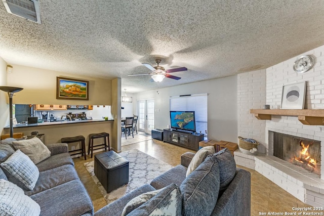 living room with ceiling fan, a fireplace, light tile patterned flooring, and a textured ceiling