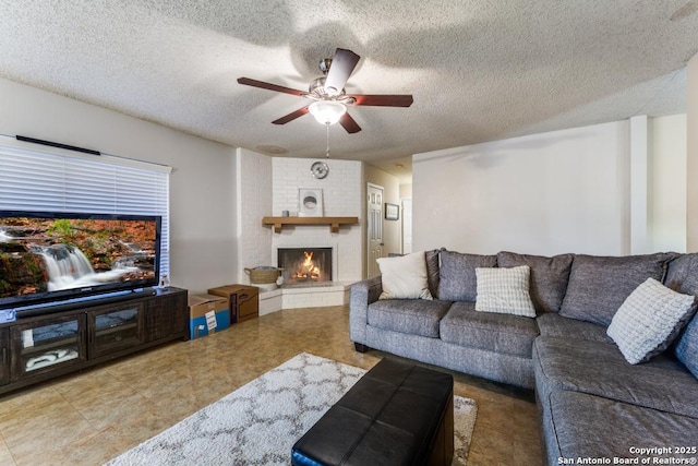 living room with ceiling fan, a textured ceiling, and a brick fireplace