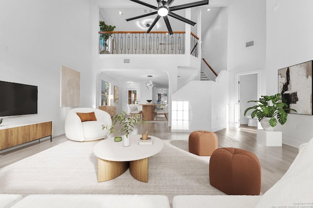 living room featuring plenty of natural light, high vaulted ceiling, wood-type flooring, and ceiling fan with notable chandelier