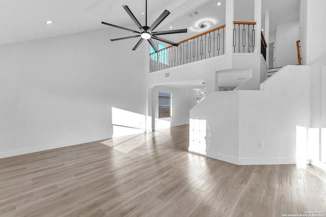 unfurnished living room featuring ceiling fan, a towering ceiling, and light hardwood / wood-style floors