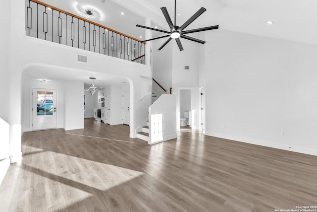 unfurnished living room featuring ceiling fan, wood-type flooring, and a high ceiling