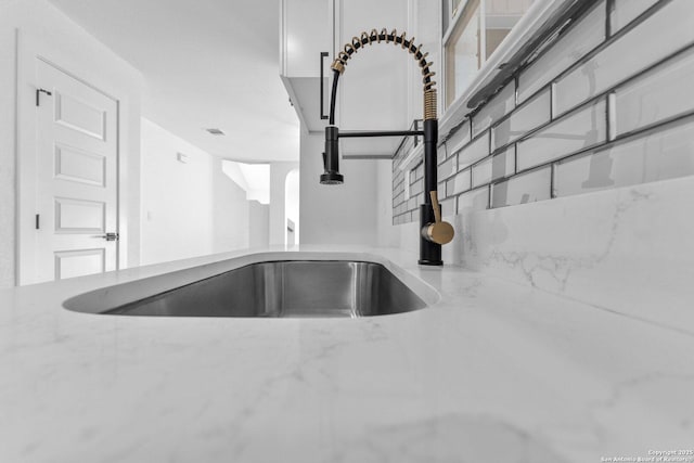 details featuring backsplash, light stone countertops, and sink