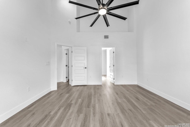 interior space with ceiling fan, light hardwood / wood-style floors, and a towering ceiling