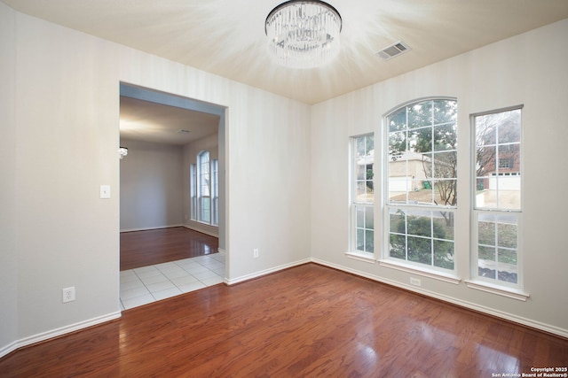 empty room featuring light hardwood / wood-style flooring, a wealth of natural light, and a notable chandelier