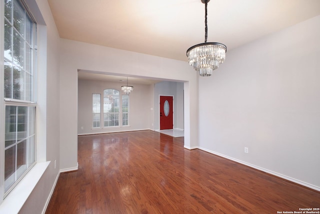 empty room with a notable chandelier and dark hardwood / wood-style flooring