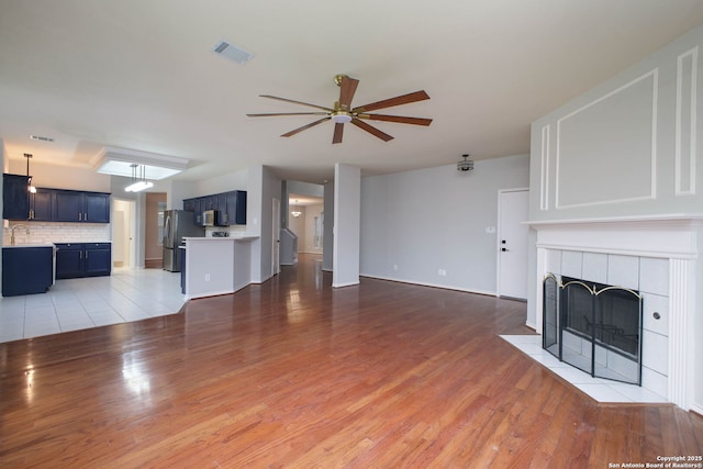 unfurnished living room with a tile fireplace, hardwood / wood-style flooring, and ceiling fan