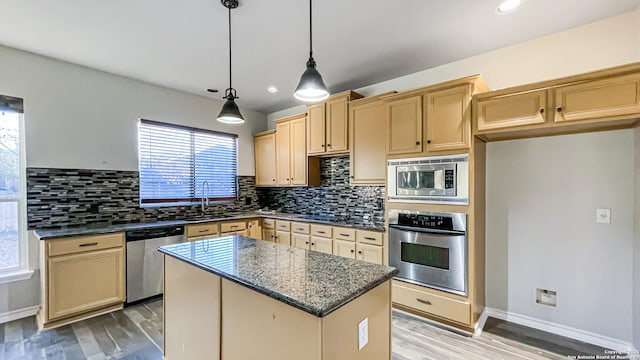 kitchen with sink, hanging light fixtures, dark stone counters, a kitchen island, and appliances with stainless steel finishes