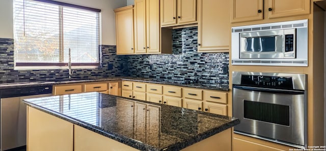 kitchen with appliances with stainless steel finishes, a kitchen island, dark stone counters, and sink