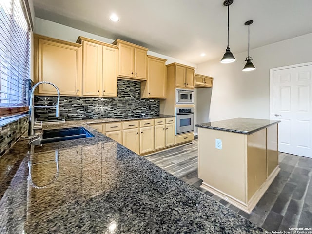 kitchen with light brown cabinets, dark stone counters, hanging light fixtures, sink, and appliances with stainless steel finishes