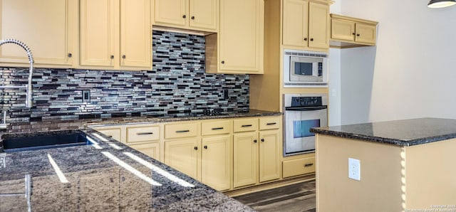 kitchen with backsplash, dark hardwood / wood-style flooring, dark stone countertops, and stainless steel appliances