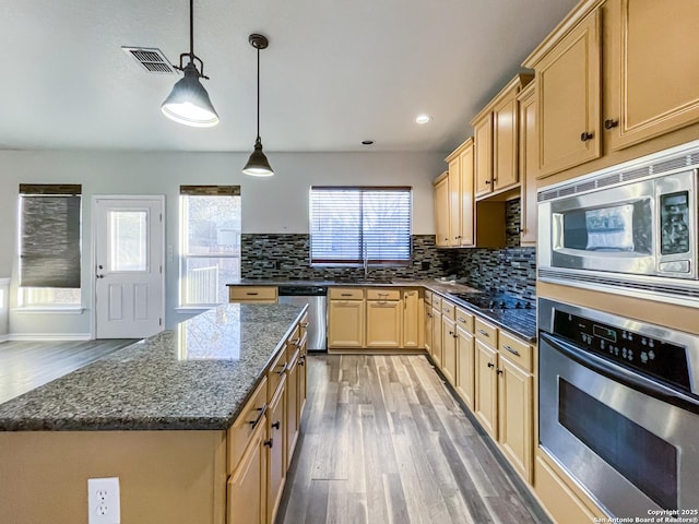 kitchen featuring pendant lighting, dark stone counters, light hardwood / wood-style flooring, a kitchen island, and stainless steel appliances