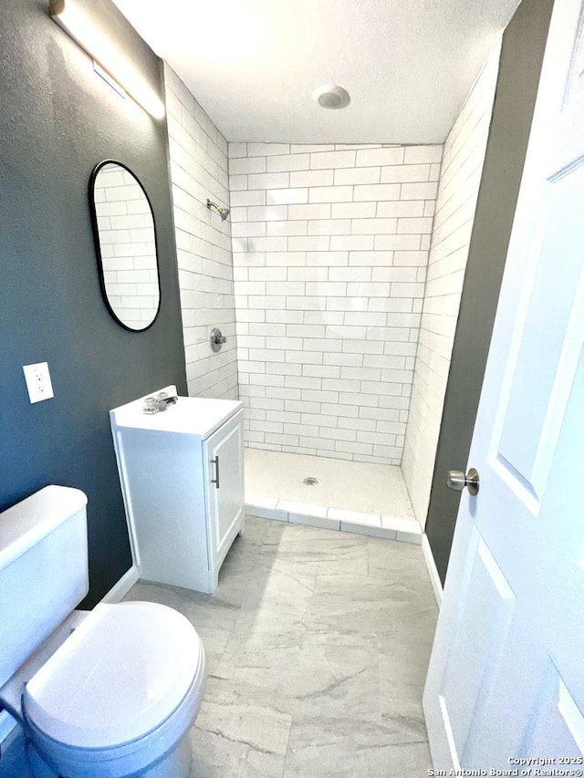 bathroom with a tile shower, vanity, a textured ceiling, and toilet