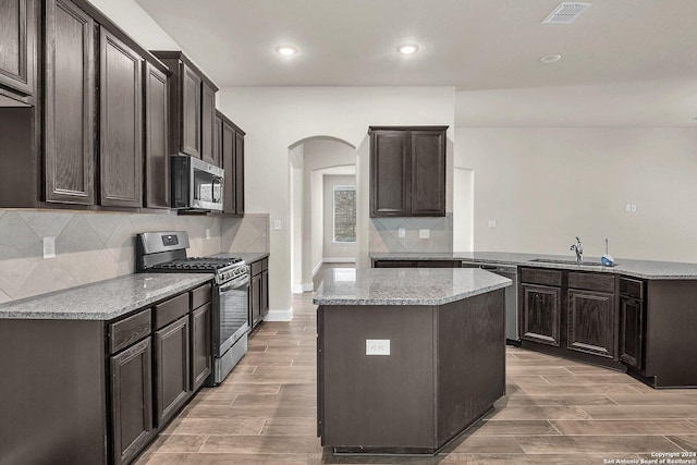 kitchen featuring sink, light stone countertops, light wood-type flooring, appliances with stainless steel finishes, and a kitchen island