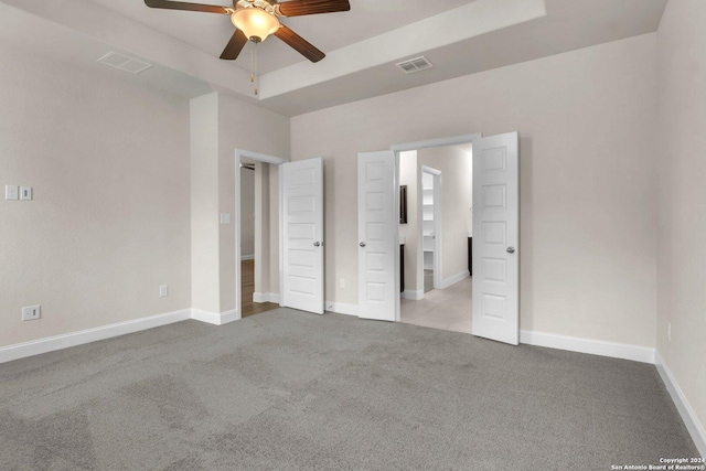 unfurnished bedroom featuring ceiling fan, a raised ceiling, and light colored carpet