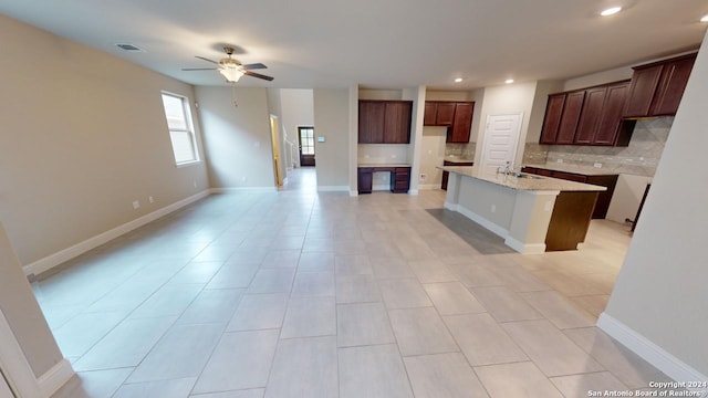 kitchen featuring light stone countertops, sink, ceiling fan, tasteful backsplash, and an island with sink