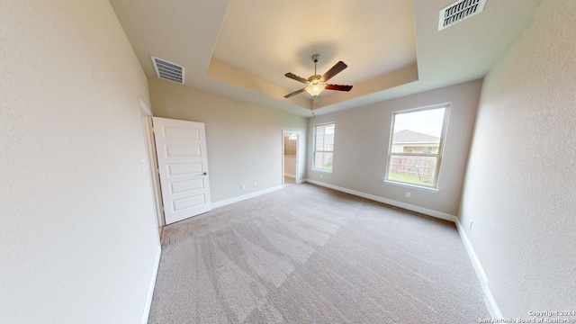 empty room featuring a tray ceiling, ceiling fan, and light colored carpet