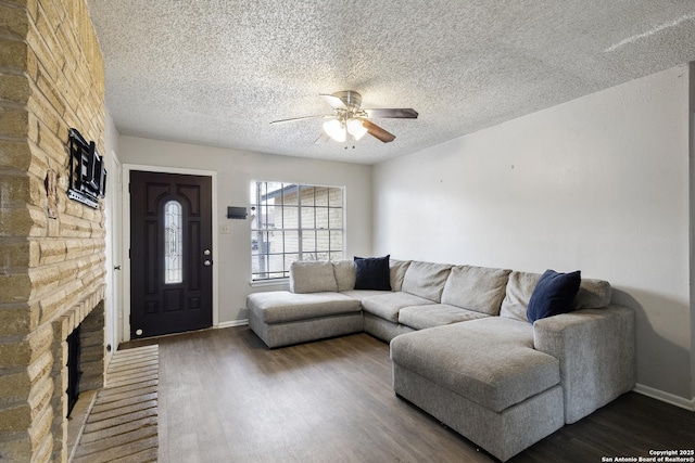 living room featuring ceiling fan, dark wood-type flooring, a fireplace, and a textured ceiling