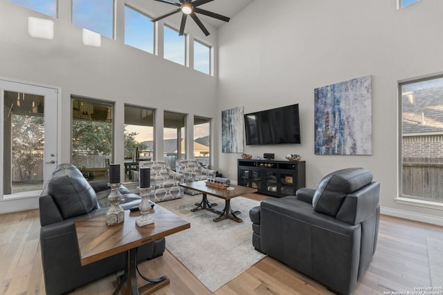 living room with ceiling fan, light hardwood / wood-style flooring, and a towering ceiling