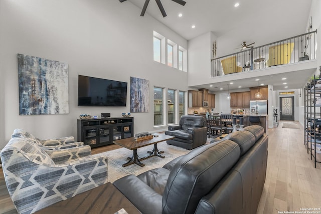 living room with ceiling fan, a high ceiling, and light hardwood / wood-style flooring