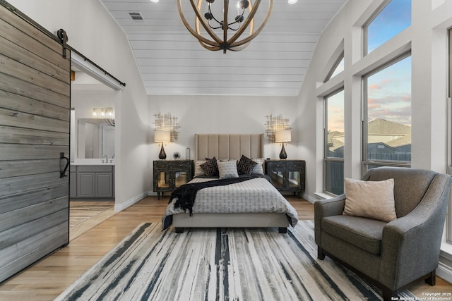 bedroom with light hardwood / wood-style flooring, ensuite bath, a barn door, a notable chandelier, and wood ceiling