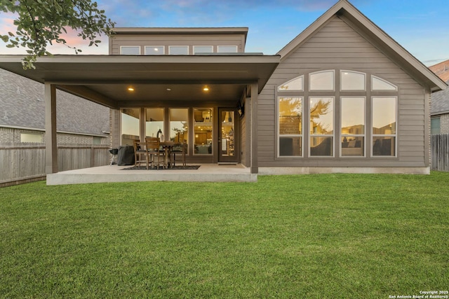 back house at dusk featuring a patio area and a lawn