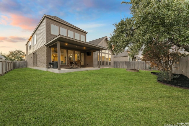 back house at dusk with a lawn and a patio