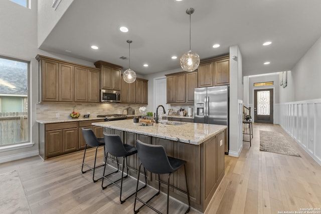 kitchen with sink, stainless steel appliances, light hardwood / wood-style floors, decorative light fixtures, and a center island with sink