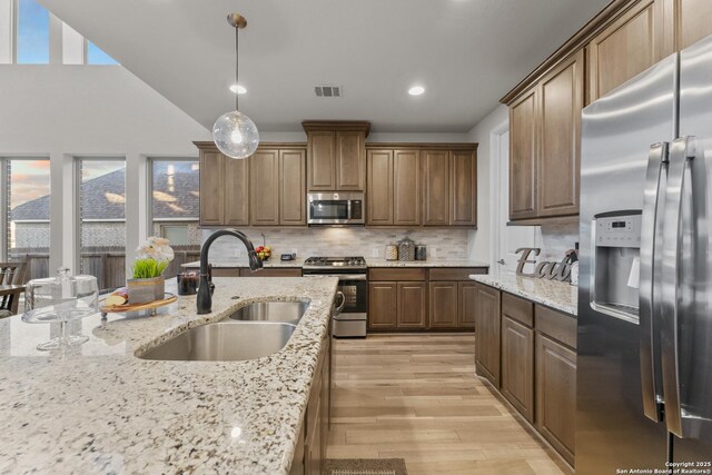 kitchen featuring appliances with stainless steel finishes, tasteful backsplash, light stone counters, sink, and decorative light fixtures