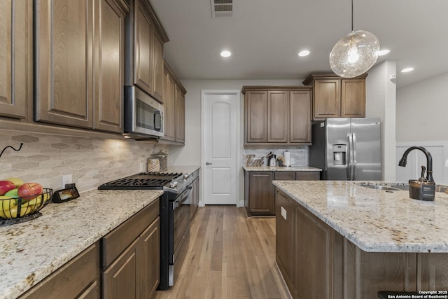 kitchen featuring decorative backsplash, light stone counters, sink, and appliances with stainless steel finishes